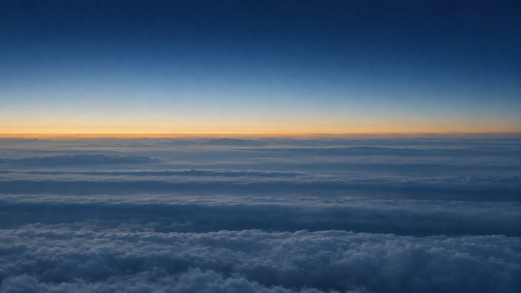 A calm layered cloud deck at first light, seen from above